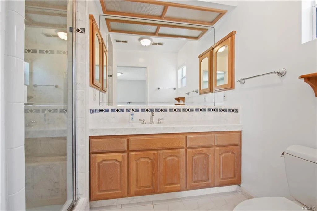 Bathroom with wooden cabinets and a glass shower.