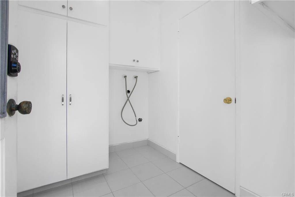 Empty white laundry room with a sink and cabinets.
