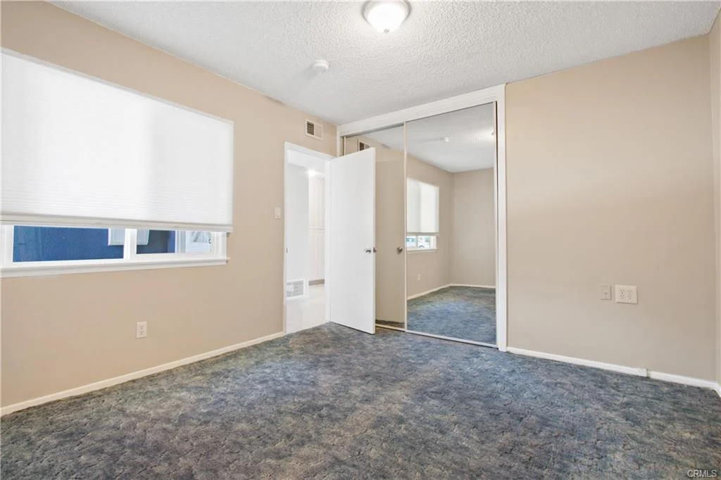 Room with beige walls, blue carpet, mirror closet door, and window with blinds