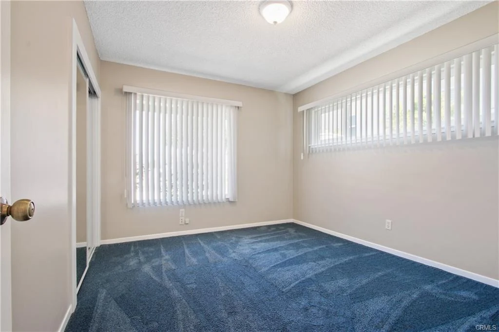 Room with blue carpet, light walls, window with blinds, shelf, and open door
