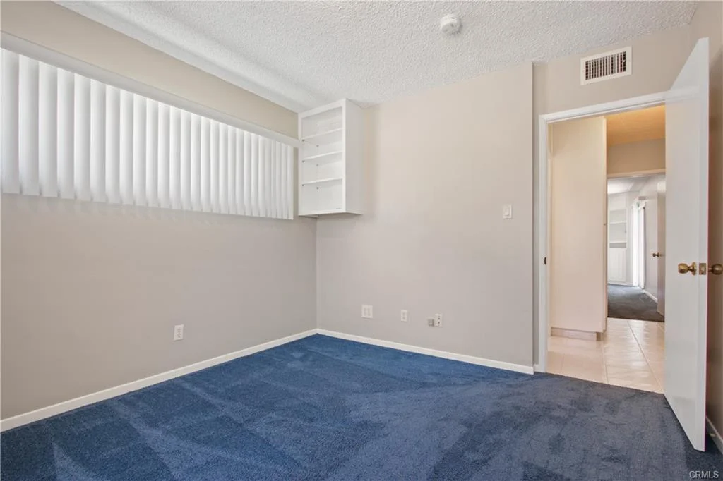 Room with blue carpet, light walls, window with blinds, shelf, and open door