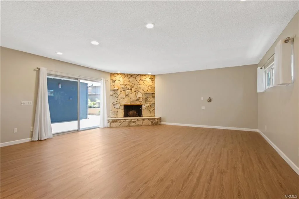Empty room with wood floors and a stone fireplace.