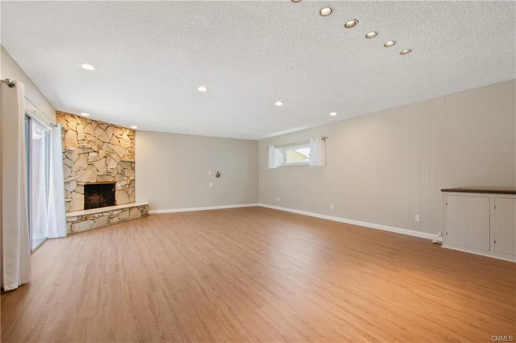 Empty room with wood floors and a stone fireplace.
