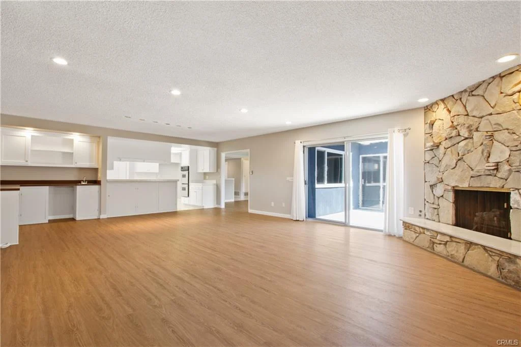 Empty room with wood floors and a stone fireplace.
