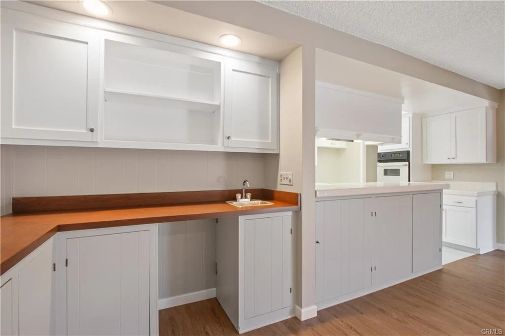 White kitchen with wood countertops and white appliances.