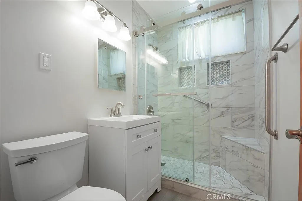 bathroom with a toilet, sink vanity, and a glass shower with marble tiles.