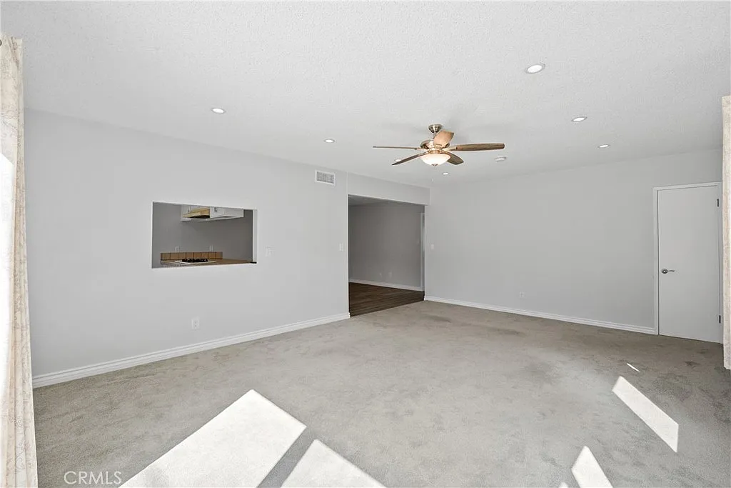 room with gray walls, a ceiling fan, carpet, and a view of the kitchen.