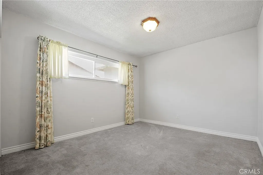 Empty room with light walls, carpet, window curtains, and a ceiling light.