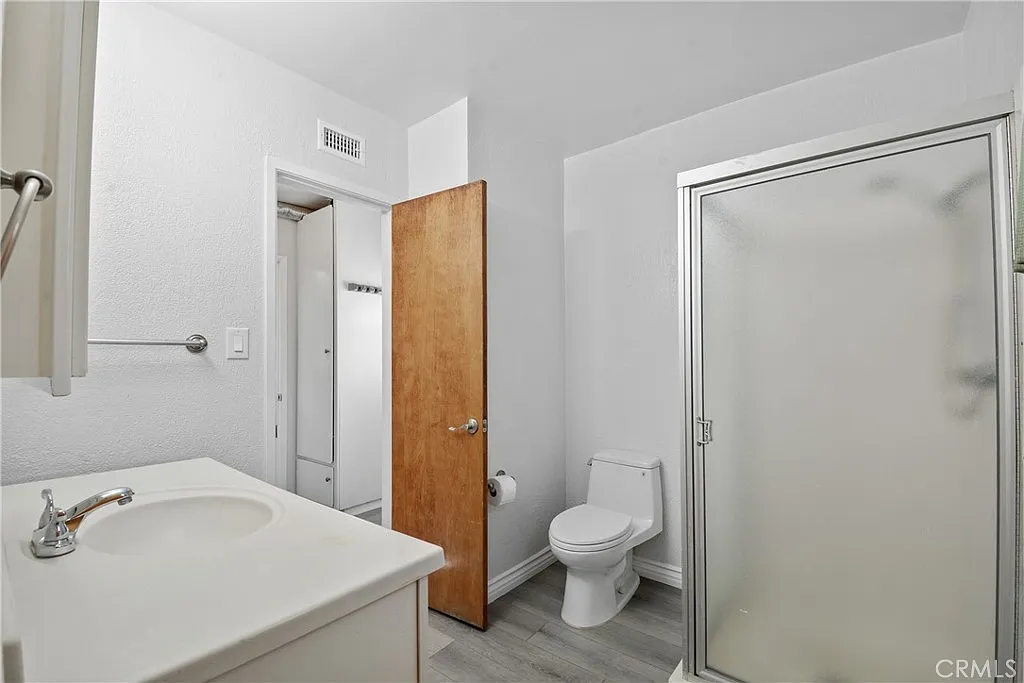 bathroom with white walls, a shower with a glass door, a toilet, and a sink with a silver faucet.