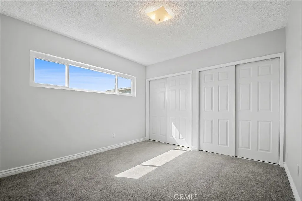 Empty room with gray walls, gray carpet, a window, and large white closet doors.