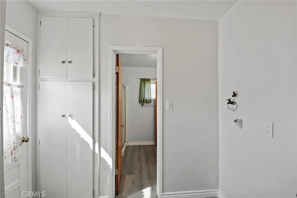 white hallway with a built-in cupboard and a door showing a green curtain and wood floor.