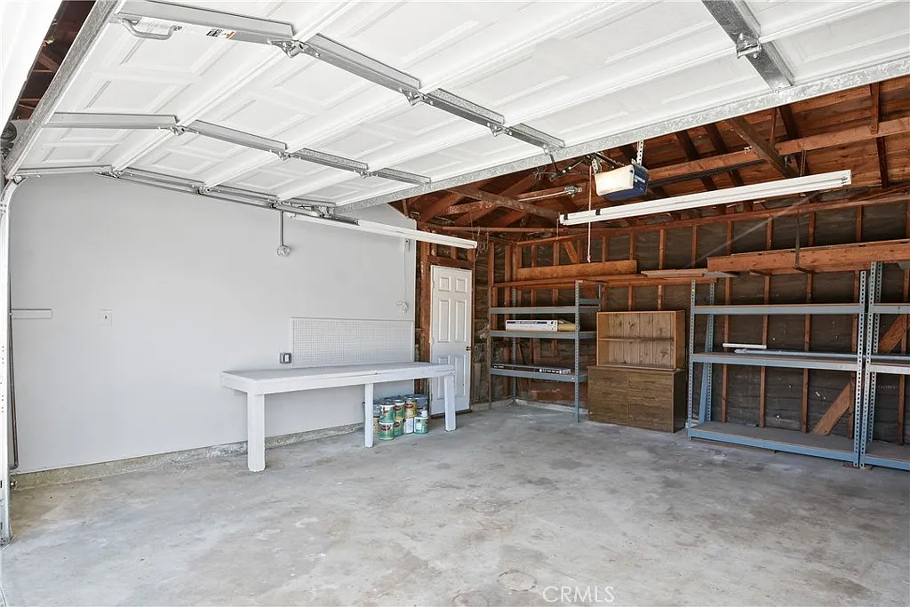 Clean garage with a flat floor, white walls, and open wooden beams with lights.