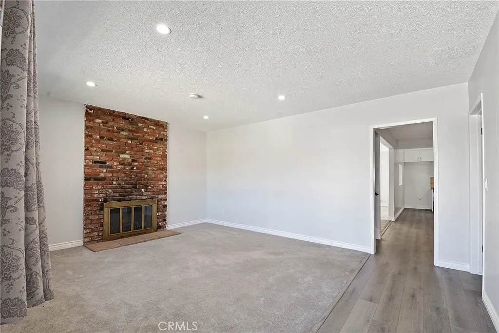 Living room with a brick fireplace, light-colored walls, modern lighting, and a doorway.