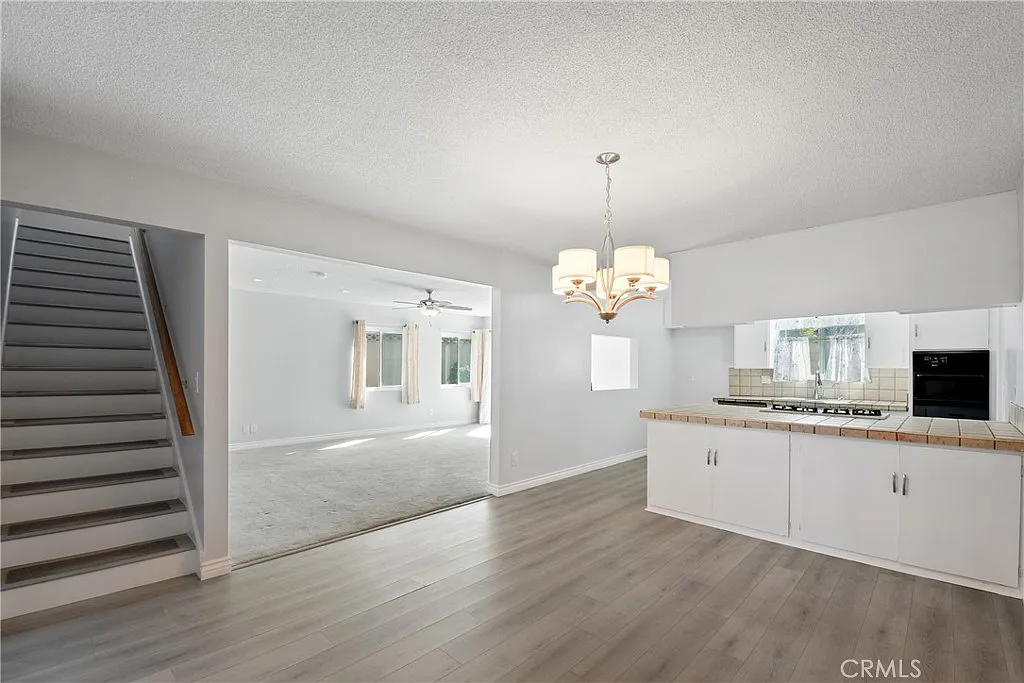 living space with a staircase, white kitchen cabinets, a chandelier, and light-colored flooring.