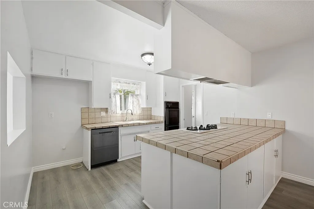 kitchen with white cabinets, a gas stove, tiled countertops, and a dining area.