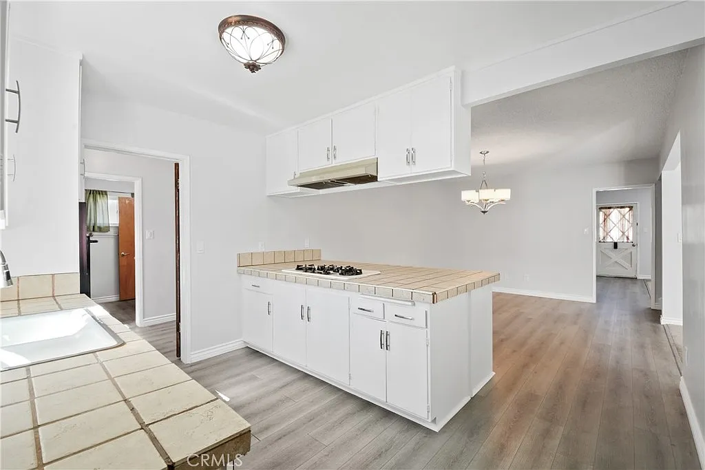 kitchen with white cabinets, tiled countertops, a gas stove, and a dining area with a chandelier.