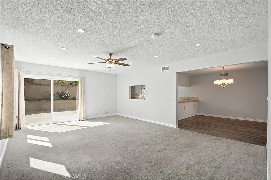 living area with a ceiling fan, sliding glass doors, a dining area with a chandelier, and carpet.