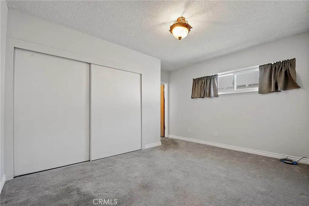 Empty room with carpet, a ceiling light, two closet doors, and a window with curtains.
