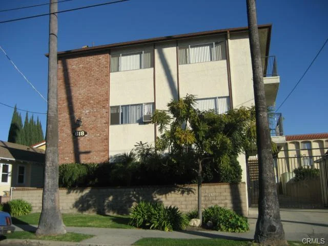 Building with brick walls, balconies, windows, palm trees, shrubs, and walkway