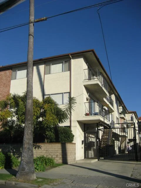Building with white exterior, balconies, gate, palm trees, and greenery