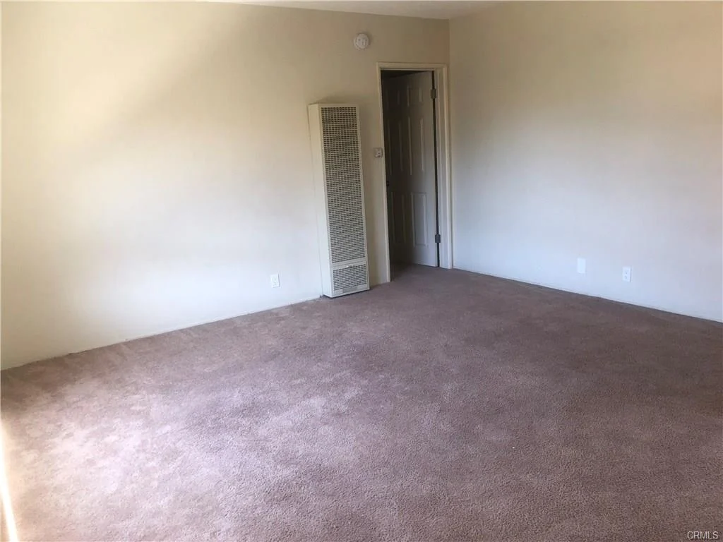 Empty room with light walls, carpet floor, vent, and door