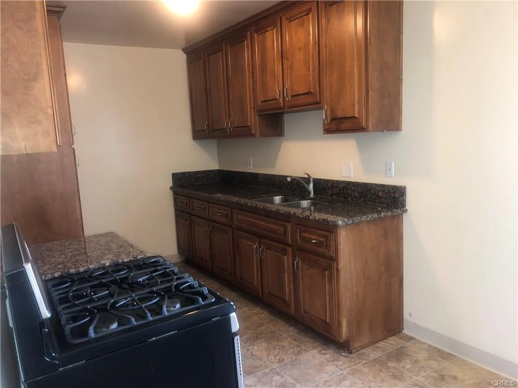 Kitchen with wood cabinets, granite counter, sink, and gas stove