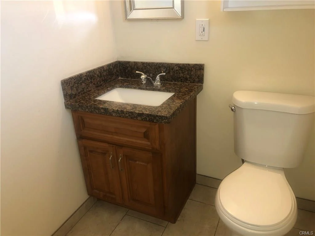 Bathroom with wood cabinet, granite counter, sink, and toilet
