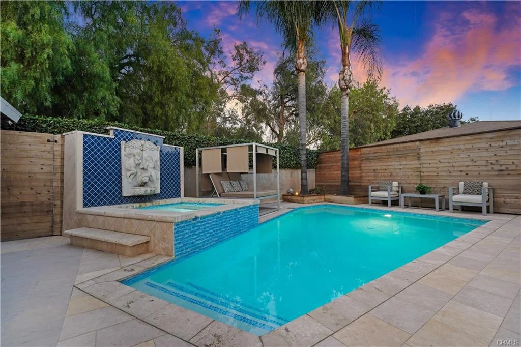 Backyard with a pool, a jacuzzi, wooden fence, and green plants around.
