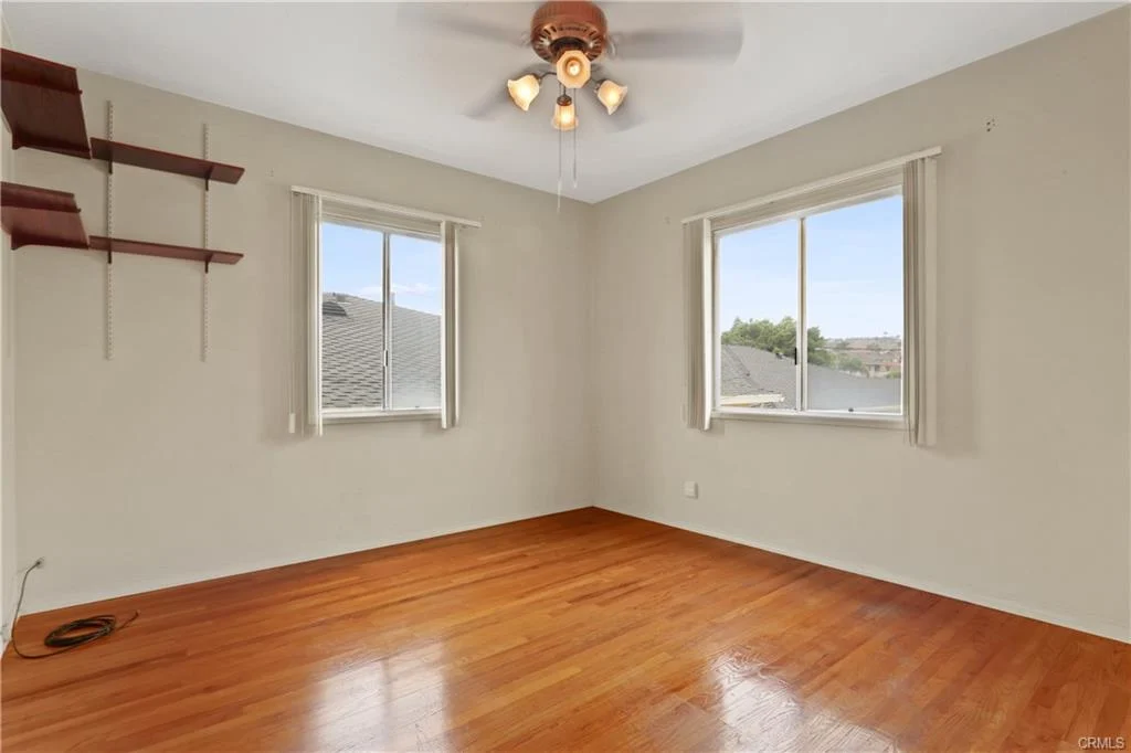 Room with wood floors, a ceiling fan, and shelves.