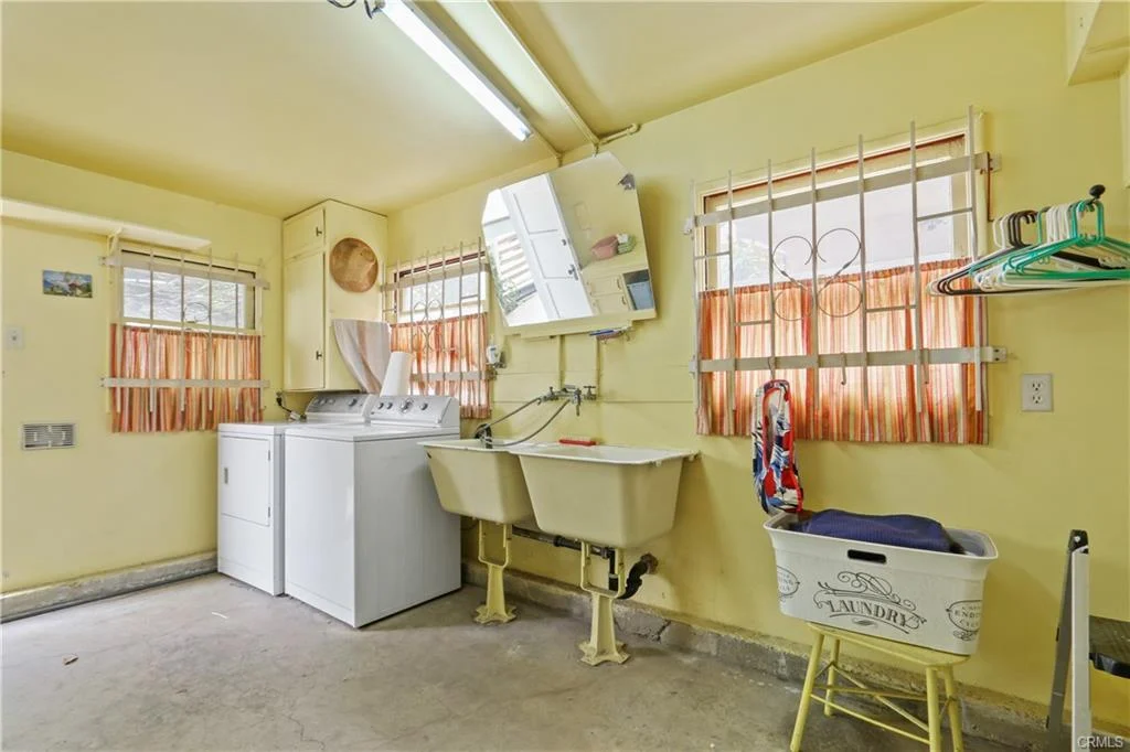 Yellow laundry room with a washer, sink, and drying rack.
