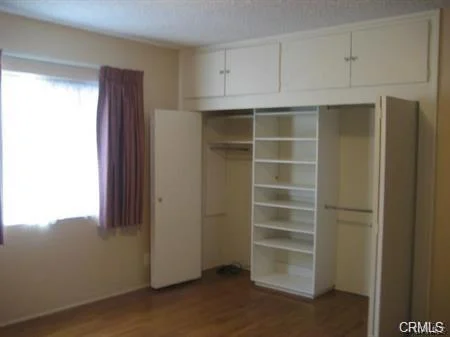 Bedroom with window, beige walls, wood floor, closet, and built-in cabinets