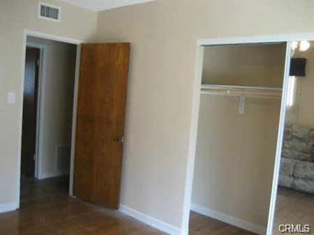 Room with wooden door, open closet with clothes, and beige walls