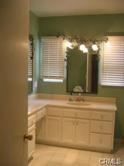 Bathroom with sink, mirror, white cabinets, windows, and door