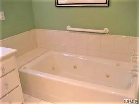 Bathroom with bathtub, grab bar, light green walls, and storage