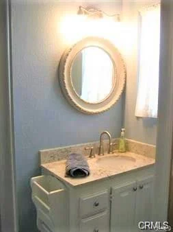Bathroom with sink, circular mirror, white cabinets, and window