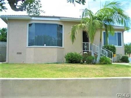 Single-story house California real estate with large front window, palm tree, and well-kept lawn