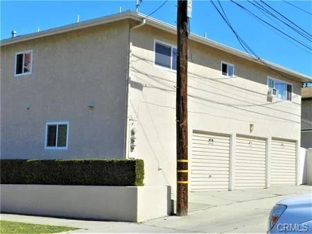 Beige apartment building with windows, garage doors, and front hedge