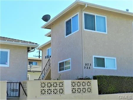 Two-story beige apartment building with windows, staircase, satellite dish, and landscaped front area