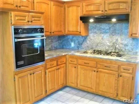 Kitchen with wooden cabinets, built-in oven, gas stove, and granite countertops