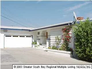House with white exterior walls, a driveway, a garage, and greenery in front.