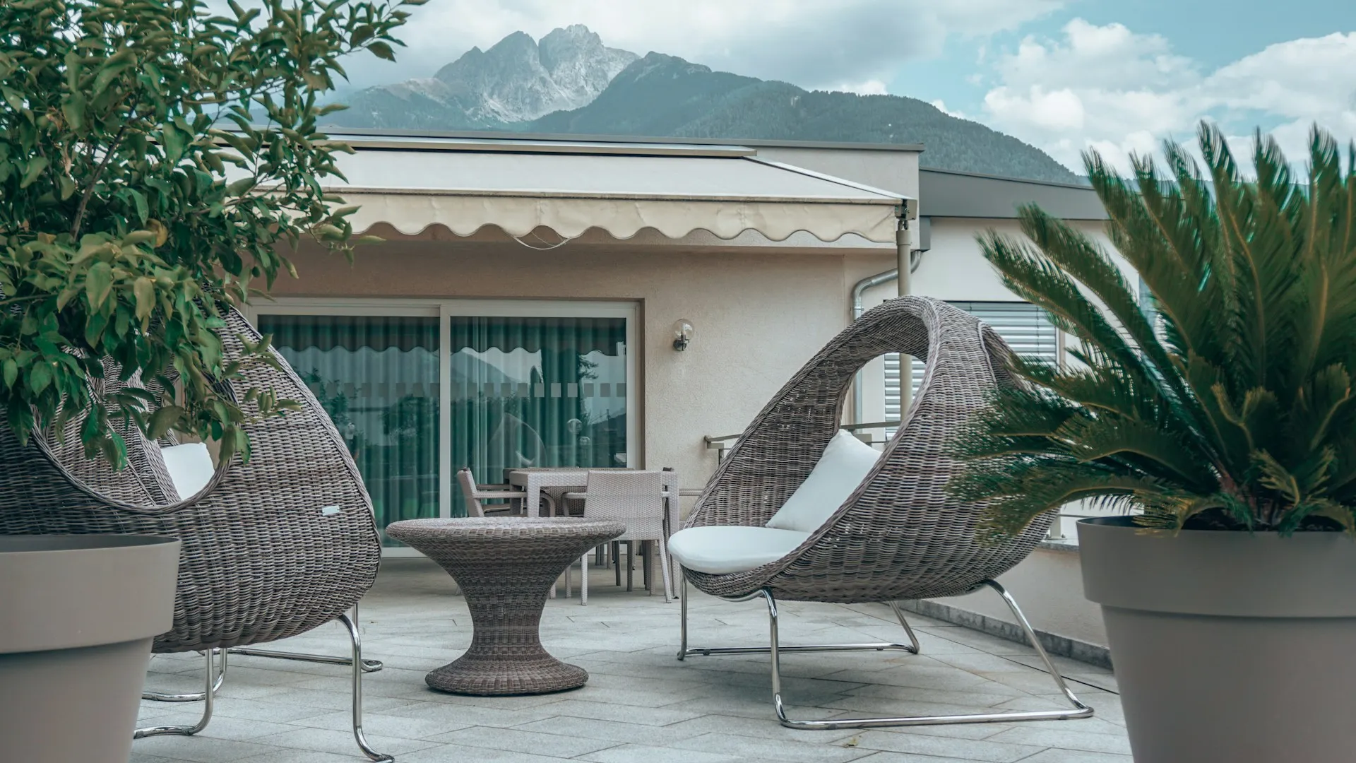 Terrace with two big chairs, a small table, plants, and mountains in the background.