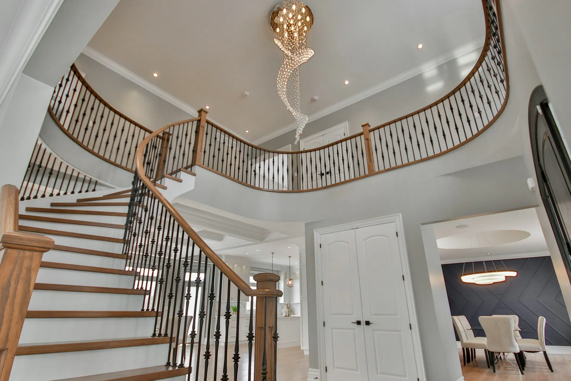 Room with a curved wooden staircase, black railings, and a hanging light.
